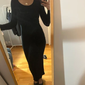 Svart långklänning - Elegant svart långklänning med långärmad design. Klänningen har en tight passform som framhäver figuren och är perfekt för en stilren look.