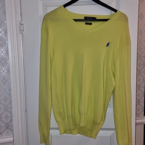 Gul tröja från Ralph Lauren - Säljer en stilren gul tröja från Ralph Lauren i slim fit. Tröjan är tillverkad av mjuk pima bomull och har en v-ringad hals. Den har långa ärmar och en broderad blå logotyp på bröstet. Perfekt för en snygg och bekväm look!