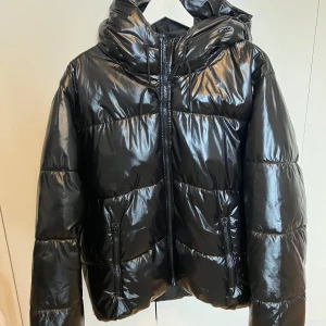 Svart glansig pufferjacka - Snygg svart pufferjacka med glansig yta. Finns inga tecken på användning då den inte används så mycket. Toppen skick