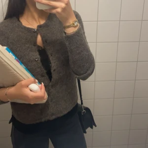 Grå kofta med knappar - Mysig brun kofta med knappar framtill. Perfekt för kyligare dagar och enkel att matcha med olika outfits. Koftan har en klassisk design med rund hals och långa ärmar.