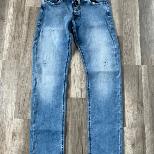 Blå jeans från Jack & Jones - Snygga blå jeans från Jack & Jones i modellen Slim/Glenn. De har en klassisk femficksdesign och en lätt slitning för en cool look. Perfekta för en avslappnad stil.