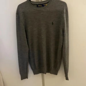 Stickad tröja från Polo Ralph Lauren - Snygg grå tröja från Polo Ralph Lauren i tvättbar merinoull. Tröjan har en slim fit passform och är långärmad. Perfekt för en stilren look.