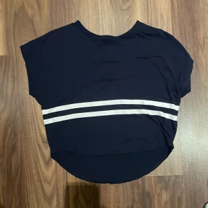 Mörkblå topp  - Säljer en mörkblå topp från H&M med två vita ränder. Toppen har en lös passform och korta ärmar. 