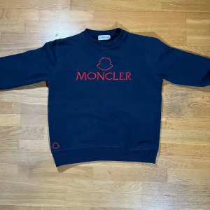 Moncler tröja - Det står på den att den är s men skulle nog sig att den är mer som xs. Snygg mörkblå sweatshirt från Moncler med röd logotyp på bröstet. Tröjan har långa ärmar och ribbade muddar vid ärmslut och nederkant. Perfekt för en stilren och bekväm look. Är en replika.