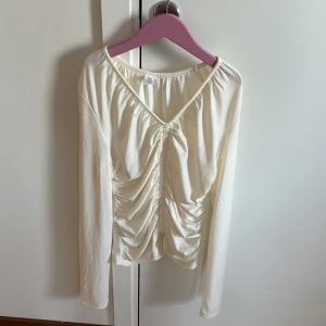 Vit långärmad topp från C.W.M - Säljer en stilren vit långärmad topp från C.W.M med rynkade detaljer framtill. Toppen har en v-ringad design och är tillverkad i ett mjukt material som ger en bekväm passform. Perfekt för både vardag och speciella tillfällen.