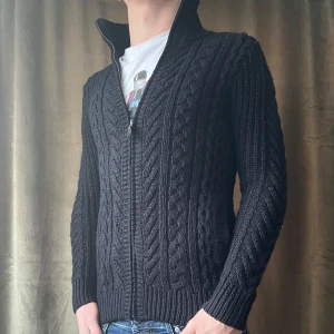 Svart Kofta  - Snygg svart stickad tröja från Superdry med dragkedja och hög krage. Perfekt för kyliga dagar med sitt stilrena flätmönster och ribbade muddar. Vid minsta fråga eller fundering hör av er🤝