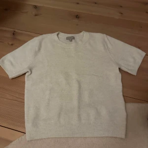 Vit kortärmad tröja - Säljer en stilren vit tröja med korta ärmar. Perfekt för en avslappnad look. Tröjan har en rund hals och ribbade kanter vid ärmslut och nederkant.