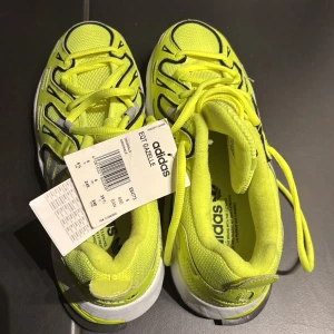 Neongula sneakers från Adidas - Snygga neongula Adidas sneakers med svarta och vita detaljer. Skorna har snörning och en bekväm sula, perfekt för en sportig look.