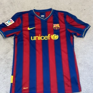 FC Barcelona fotbollströja - Säljer en klassisk FC Barcelona fotbollströja från Nike med rödblå ränder och Unicef-logga. Tröjan har korta ärmar och nummer 10 på ryggen. Perfekt för alla Barça-fans!