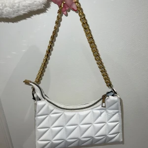 Vit quiltad axelväska med guldkedja - Snygg vit axelväska i quiltat mönster med en elegant guldkedja som axelrem. Väskan är i mycket bra skick och har använts endast 2-3 gånger. 