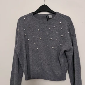 Grå stickad tröja med pärlor - Snygg grå stickad tröja från hm med dekorativa pärlor på framsidan. Tröjan har långa ärmar och en rund halsringning. Perfekt för en stilren look.
