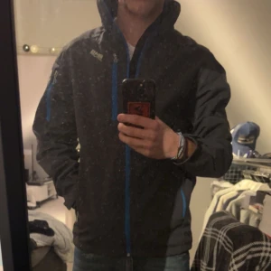 Grå jacka från 8848 Altitude - Säljer en grå jacka från 8848 Altitude med blåa dragkedjor och flera praktiska fickor. Perfekt för utomhusaktiviteter med sin funktionella design.