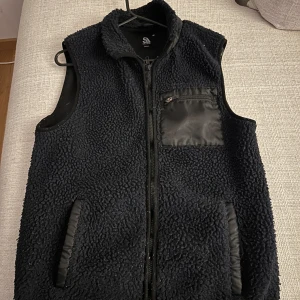 Svart fleeceväst med dragkedja - Säljer en svart fleeceväst med dragkedja och praktiska fickor. Västen har en bröstficka med dragkedja och är perfekt för kyligare dagar. Köparen står för frakt!
