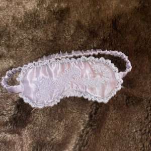 Pastell Lila siden sovmask med spetsdetaljer - Elegant ljus lila sovmask i siden med vackra spetsdetaljer runt kanterna. Perfekt för en god natts sömn eller en avkopplande stund. Ganska liten i huvudmått. Den är köpt i frankerike