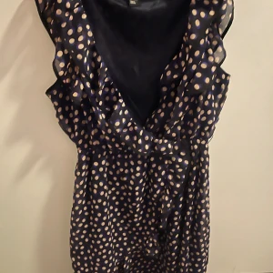 Prickig klänning med volangdetaljer (SWISH ENDAST!) - Snygg prickig klänning i mörkblått med vita prickar. Den har volangdetaljer längs den v-ringade halsen och är ärmlös. Perfekt för en somrig look!