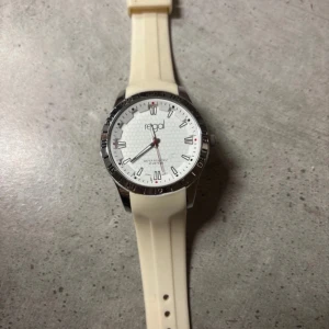 Vit klocka från Regal - Snygg vit klocka från Regal med en stilren urtavla och tydliga markeringar. Klockan har en ljus rem och en silverfärgad boett. Perfekt för en minimalistisk look.