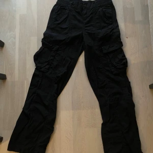 Svarta cargopants med fickor - Säljer ett par svarta cargopants med flera praktiska fickor. Byxorna har en loose passform och är perfekta för en avslappnad stil. De är tillverkade i ett slitstarkt material och har elastisk midja för extra komfort.