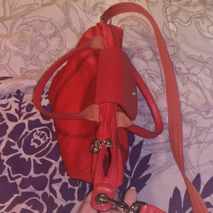 Röd Longchampväska i fint skick  - Snygg röd axelväska med praktisk dragkedja och knäppning på ovansidan . Ett innerfack för småsaker. Väskan har både handtag och en justerbar axelrem för flexibel användning. Perfekt för att bära dina dagliga nödvändigheter med stil🌺