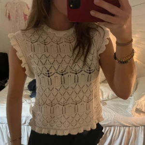 Vit spetsblus - Charmig vit spetsblus med volangdetaljer vid ärmarna och halsen. Blusen har ett vackert mönster och är perfekt för en somrig look.