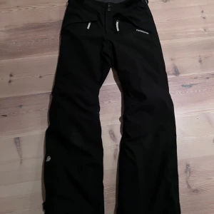 Svarta täckbyxor från Didriksons - Säljer ett par svarta skid/täckbyxor från Didriksons med dragkedja och kardborre i midjan. Perfekta för utomhusaktiviteter med sin robusta design.