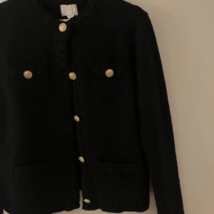 Svart kofta med guldknappar - Elegant svart kofta med dekorativa guldknappar framtill och på fickorna. Den har en klassisk design med rund hals och långa ärmar, perfekt för en stilren look. Köpt för 499, aldrig använd bara tagit av lappen🤍