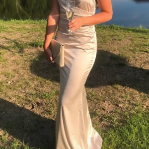 Champagnefärgad Balklänning - Superfin champagnefärgad balklänning i satin med smala axelband och öppen rygg. Perfekt för festliga tillfällen.