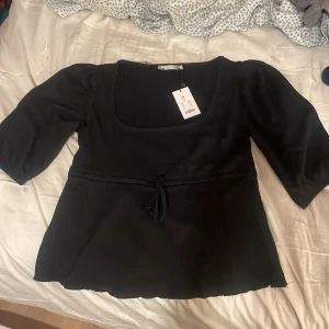 Svart topp från lager 157 - Snygg svart topp från Lager 157 med trekvartsärm och knytband i midjan. Toppen har en fyrkantig halsringning och är perfekt för en stilren look. Med prislapp 