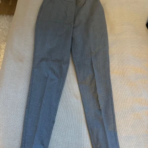 Grå rutiga byxor från BikBok - Snygga grå byxor från BikBok i storlek XS. De har ett klassiskt rutigt mönster och dragkedjor vid anklarna för en modern touch. Perfekta för både vardag och fest! 🖤