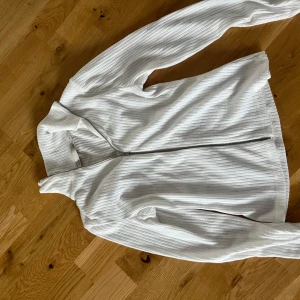 Vit ribbad jacka från 157 - Säljer en snygg vit ribbad jacka från 157 i storlek XS. Jackan har en dragkedja framtill och är långärmad. Perfekt för vår och höst när du vill ha något stilrent och bekvämt. Passar både till vardags och lite finare tillfällen. 🕊️