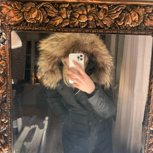 Svart dunjacka med päls från Hollies - Säljer en snygg svart dunjacka från Hollies i mycket bra skick. Jackan har en fluffig päls på huvan och knappar framtill. Perfekt för kalla vinterdagar! Den är långärmad och har en figursydd passform som håller dig varm och stilren. Pris går att diskutera 🩷