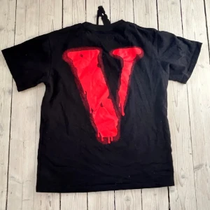 Svart t-shirt från VLone - Säljer en svart t-shirt med coolt tryck. På framsidan står det 'BAD HABITS' i vitt med 'BAD' i rött. Baksidan har ett stort rött 'V'. Perfekt för en avslappnad stil!