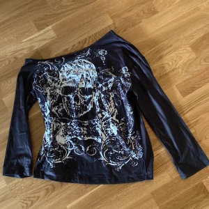 Svart långärmad topp med dödskallemotiv - Cool svart långärmad topp med ett stort vitt dödskallemotiv på framsidan. Perfekt för en edgy look och passar bra till både jeans och kjol. Materialet känns mjukt och bekvämt, perfekt för höst och vår. Toppen har en normal passform och är i mycket bra skick.