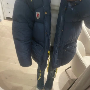 Blå dunjacka från Fjällräven - Säljer en supermysig blå dunjacka från Fjällräven i storlek XXS. Jackan har en snygg gul dragkedja. Perfekt för kalla vinterdagar. Den är i mycket bra skick och redo för nya äventyr! 💙Inga märkvärdiga defekter bara lapparna på snörerna som är slitna men enkelt att byta ut⭐️ pris kan diskuteras!