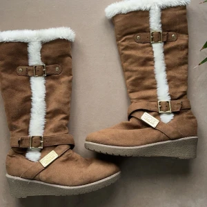 Bruna stövlar från Michael Kors - Snygga bruna stövlar från Michael Kors i mocka med vit pälsdetalj. Dem har nästan aldrig används.  De har en bekväm kilklack och dragkedja på insidan. Perfekta för höst och vinter!