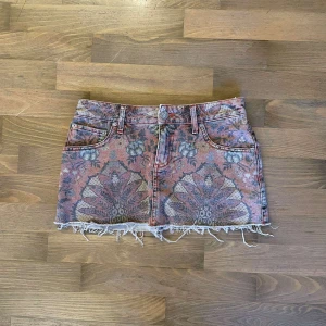 Lågmidjad jeanskjol  - Säljer en superfin kort jeanskjol med blommigt mönster i olika färger. längst ner och klassisk femficksdesign. Perfekt för sommardagar eller festivaler!