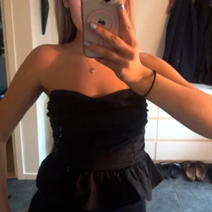 Svart axelbandslös topp  - Säljer en jätte fin topp från Nelly! Toppen har en volangdetalj vid midjan som ger en väldigt fin siluett 🥰