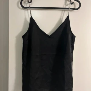 Svart linne med smala axelband - Säljer ett stilrent svart linne med smala axelband. Perfekt för både vardag och fest. Linnet har en enkel och elegant design som gör det lätt att matcha med olika outfits.