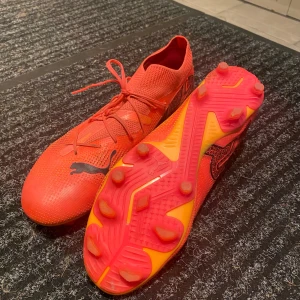 fotbollsskor från Puma - Säljer ett par snygga fotbollsskor från Puma i mycket bra skick. Skorna har en tight passform och är perfekta för fotbollsträning. De har snörning och en cool design med svarta detaljer. Sulan är utrustad med dobbar för bra grepp på planen.