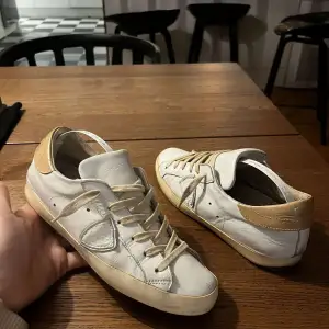 Säljer ett par vita sneakers från Philippe Model i bra skick. De har beige detaljer och snörning. Perfekta för vardagsbruk med en stilren design. Skorna är bekväma och passar till de flesta outfits. Lite slitna men fortfarande snygga och användbara!