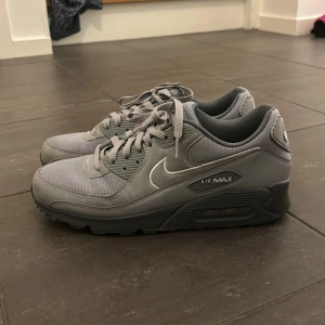 Grå Nike Air Max 90 sneakers - Säljer ett par grå Nike Air Max sneakers i mycket bra skick. De har blivit använda Max 10 gånger.  De har en stilren design med snörning och en bekväm sula. Perfekta för både vardag och träning. Storlek är inte specificerad, men de ser ut att passa en normal passform.