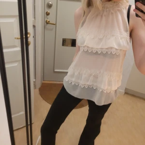 Halterneck topp med spetsdetaljer - Säljer en superfin vit/beige blus i transparent material med spetsdetaljer och volanger. Den perfekt för festliga tillfällen 💗 Blusen har en luftig passform och ger en romantisk look. Perfekt att matcha med jeans eller kostymbyxor💕