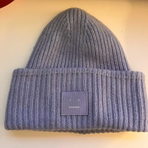 Ljusblå stickad mössa från Acne Studios - Säljer en superfin ljusblå stickad mössa från Acne Studios. Den är i 100% ull och har en ribbad design med en liten etikett framtill. Perfekt för att hålla sig varm och stilren under höst och vinter. Mössan är i mycket bra skick och passar de flesta tack vare one size-storleken.