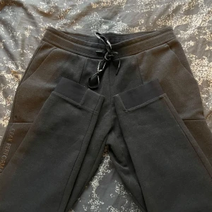 Svarta mjukisbyxor från Peak Performance - Säljer ett par svarta mjukisbyxor från Peak Performance i bra skick. De har en bekväm passform med snörning i midjan och praktiska fickor. Perfekta för en avslappnad dag eller träning. Byxorna har en diskret logga längs benet och en dragkedja på bakfickan.