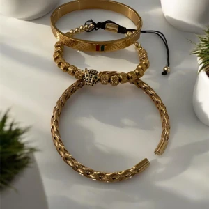 Guldfärg armband i olika stilar - Säljer tre snygga guldfärg armband i olika stilar. Ett flätat armband med elegant design, ett justerbart armband med pärlor och ett coolt lejonhuvud, samt ett slätt armband med färgglada detaljer. Perfekta för att ge din outfit en lyxig touch!
