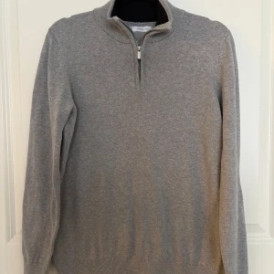 Tröja från Mango, strlk XS - En grå tröja med dragkedja i halsen. Tröjan har en hög krage och är i en mjuk och skön kvalitet. 100% bomull. Använd ett fåtal gånger. Herrstorlek XS. 