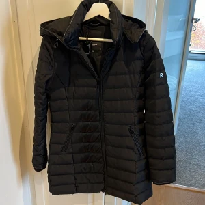 Svart dunjacka från Rockandblue - Säljer en snygg svart dunjacka från Rockandblue i storlek 34. Jackan har en stilren design med dragkedja och en mysig huva. Den är i mycket bra skick (knappt använd) och redo för nya äventyr! 🖤