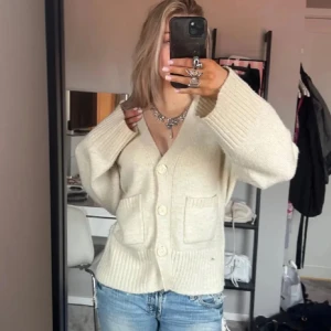 Beige kofta med knappar - Mysig beige kofta i mycket bra skick. Den har en v-ringad design med stora knappar framtill och två praktiska fickor. Perfekt för höst och vår, och ger en avslappnad men stilren look. Passar bra till jeans eller kjol.