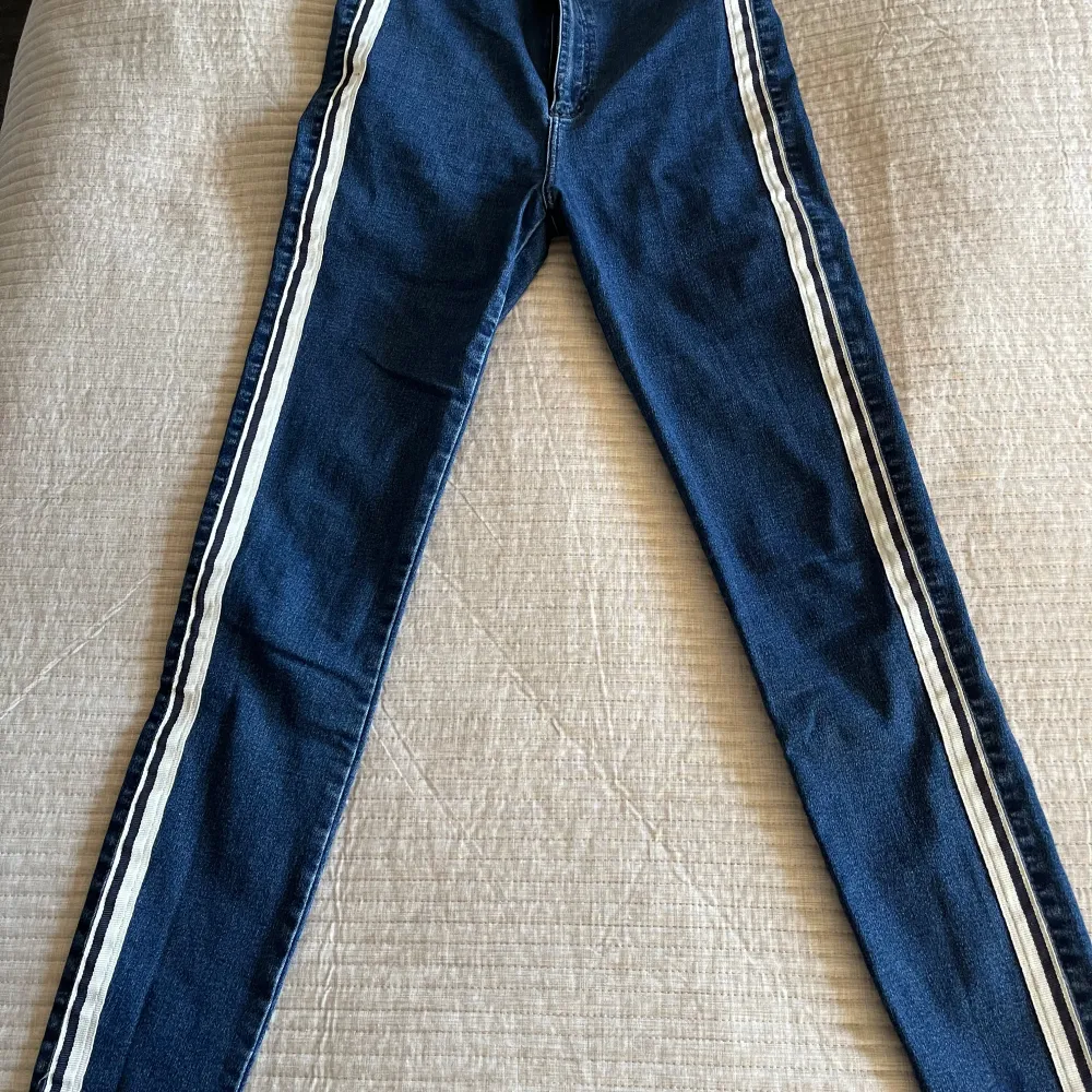 Säljer ett par snygga blå jeans från Zara Trafaluc Denim Collection. De har vita ränder längs sidorna som ger en sportig look. Perfekta för både vardag och fest! De är i bra skick och har en tight passform.. Jeans & Byxor.