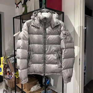 Moncler Maya - Grå Moncler Maya i fint skick, liten flaw framtill och pinhole på vänster arm samt smuts på vänster arm, går bort efter en tvätt! Syns inte mycket vid användning och överlag fint skick på knappar mm och cartoon sitter kvar. Storlek 3 passar M, kommer med moncler galge. Nypris 18.000kr mitt pris 7000kr men tar emot rimliga bud! Bara att skriva vid frågor eller funderingar, över 80 refs finns från nöjda kunder!