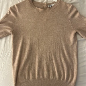 Beige tröja från Zara - Säljer en stilren beige tröja från Zara i mycket bra skick. Den har korta ärmar och en rund halsringning med knappar i nacken. Perfekt för både vår och höst! 🧡
